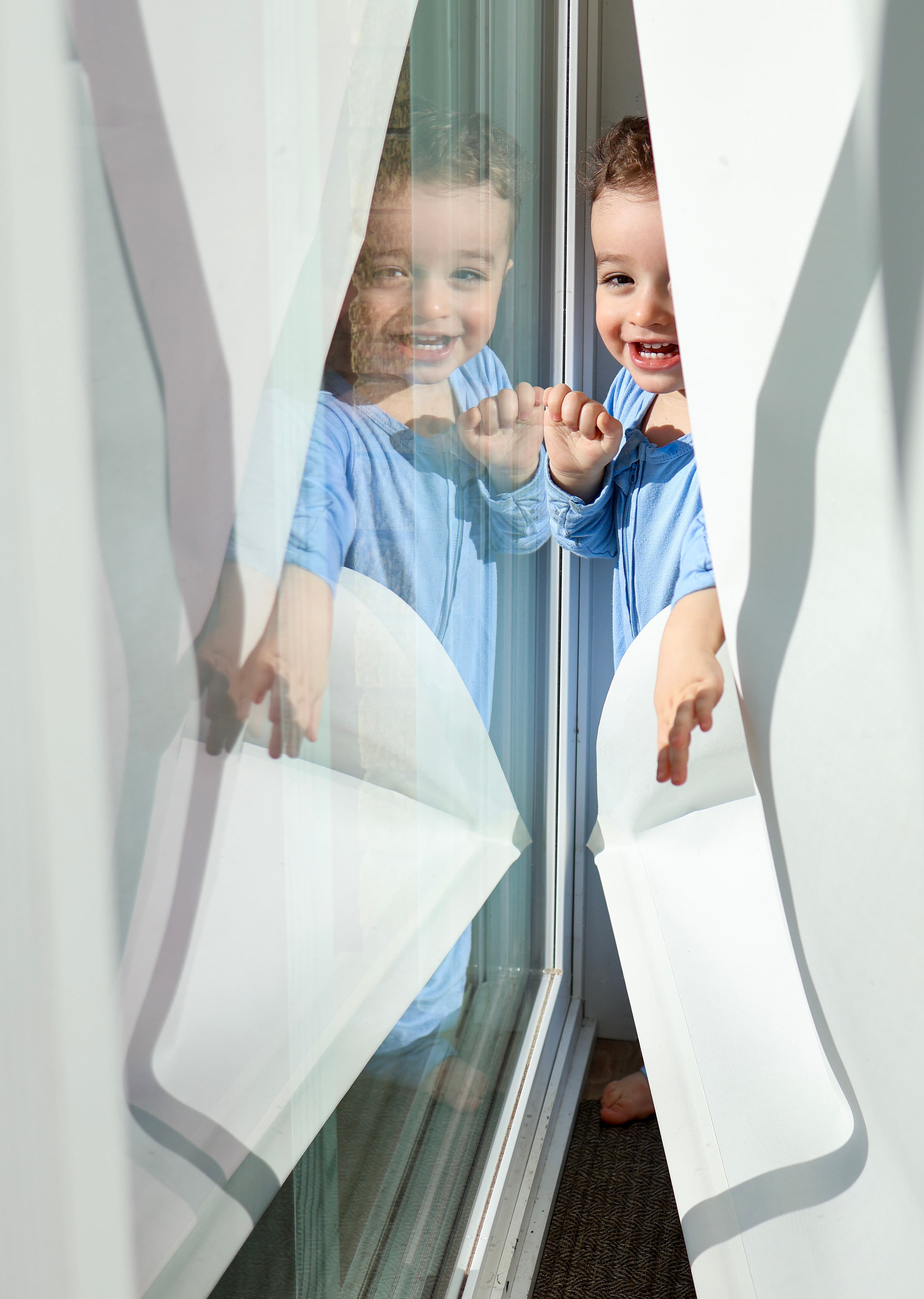 Little boy peeking out from window blinds — candid childhood photography