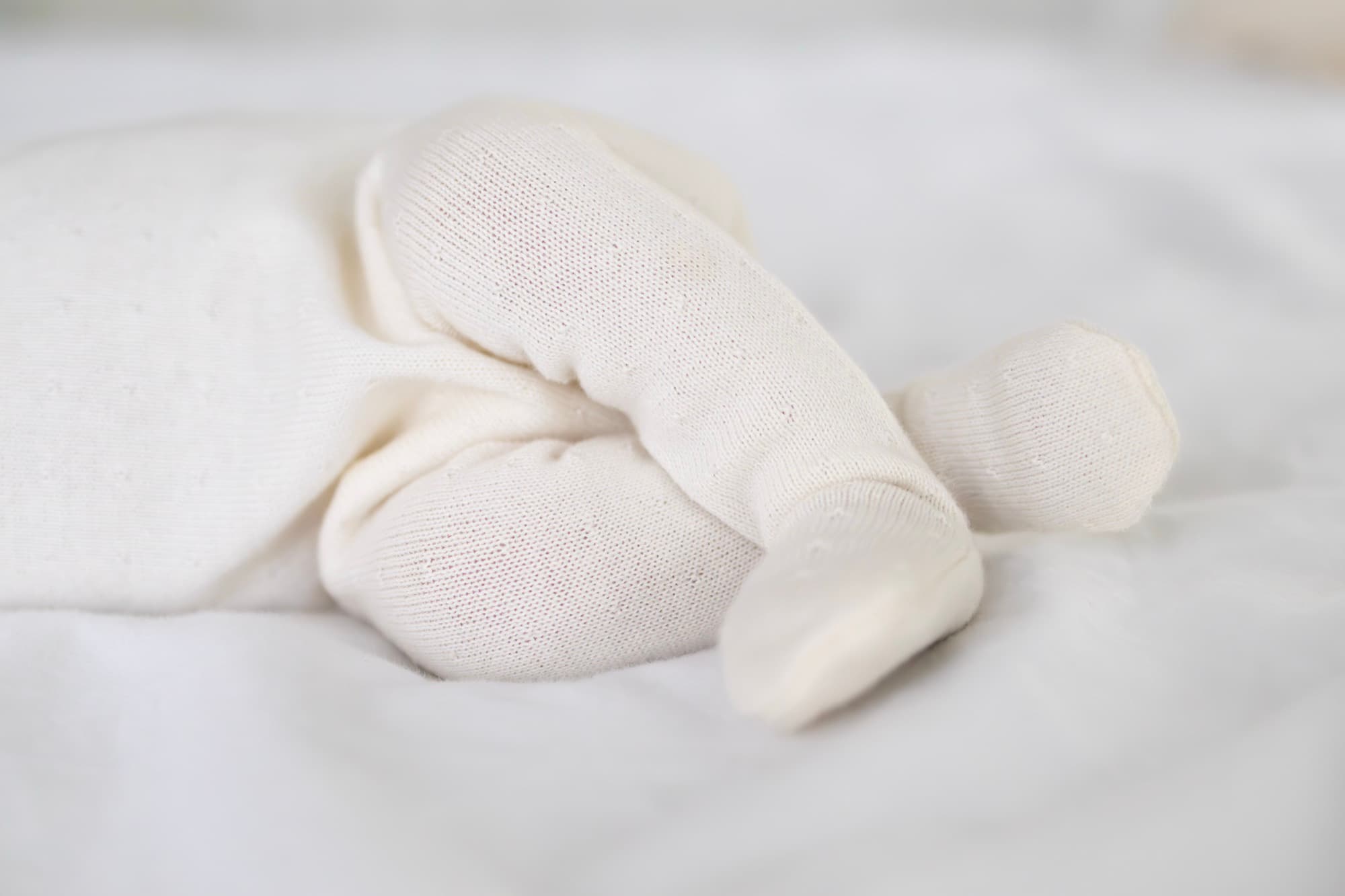 Newborn baby feet in white onesie — detail newborn photography