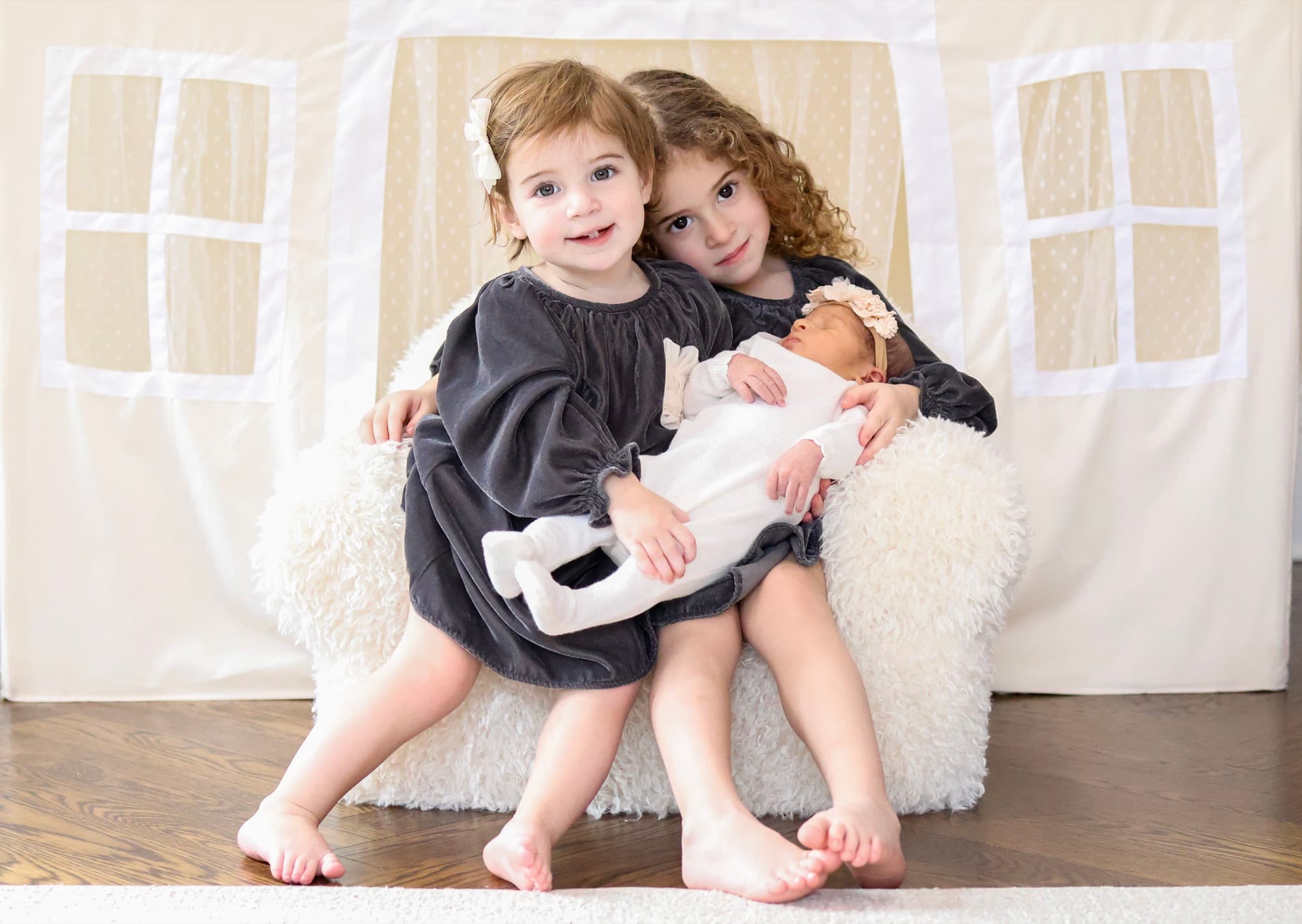 Sisters holding newborn in front of playhouse — sibling newborn photography