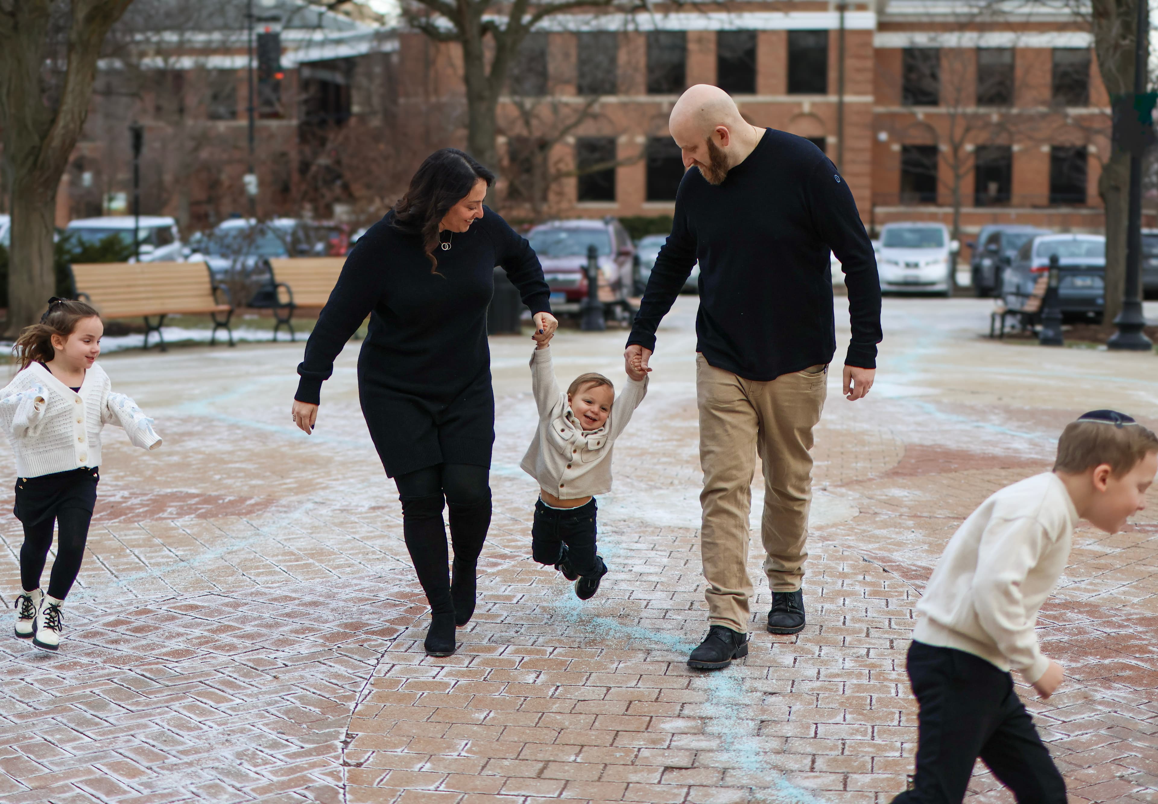 Family walking together, parents swinging toddler — playful family photography
