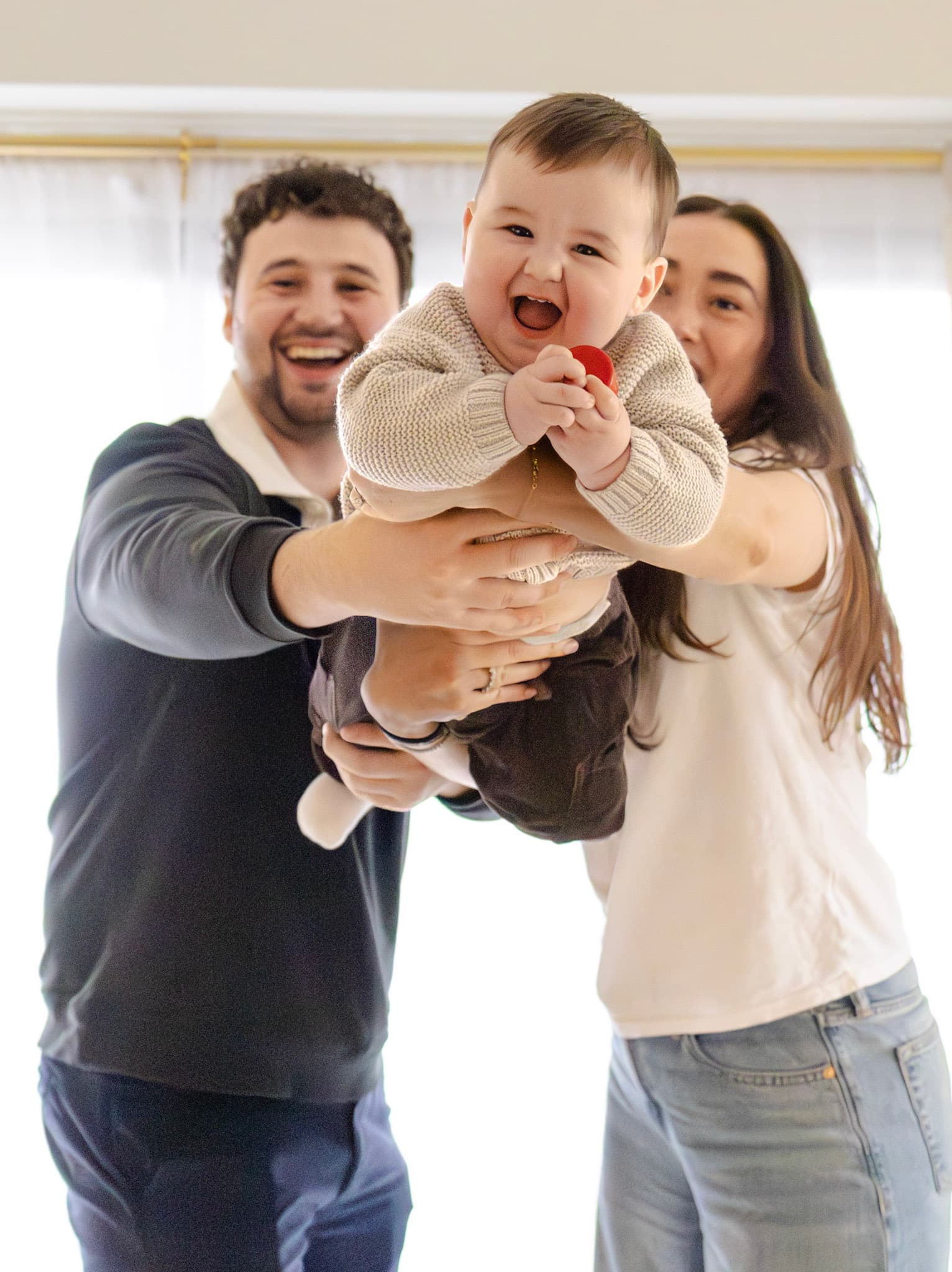 Smiling baby held toward the camera by parents during an in-home family session
