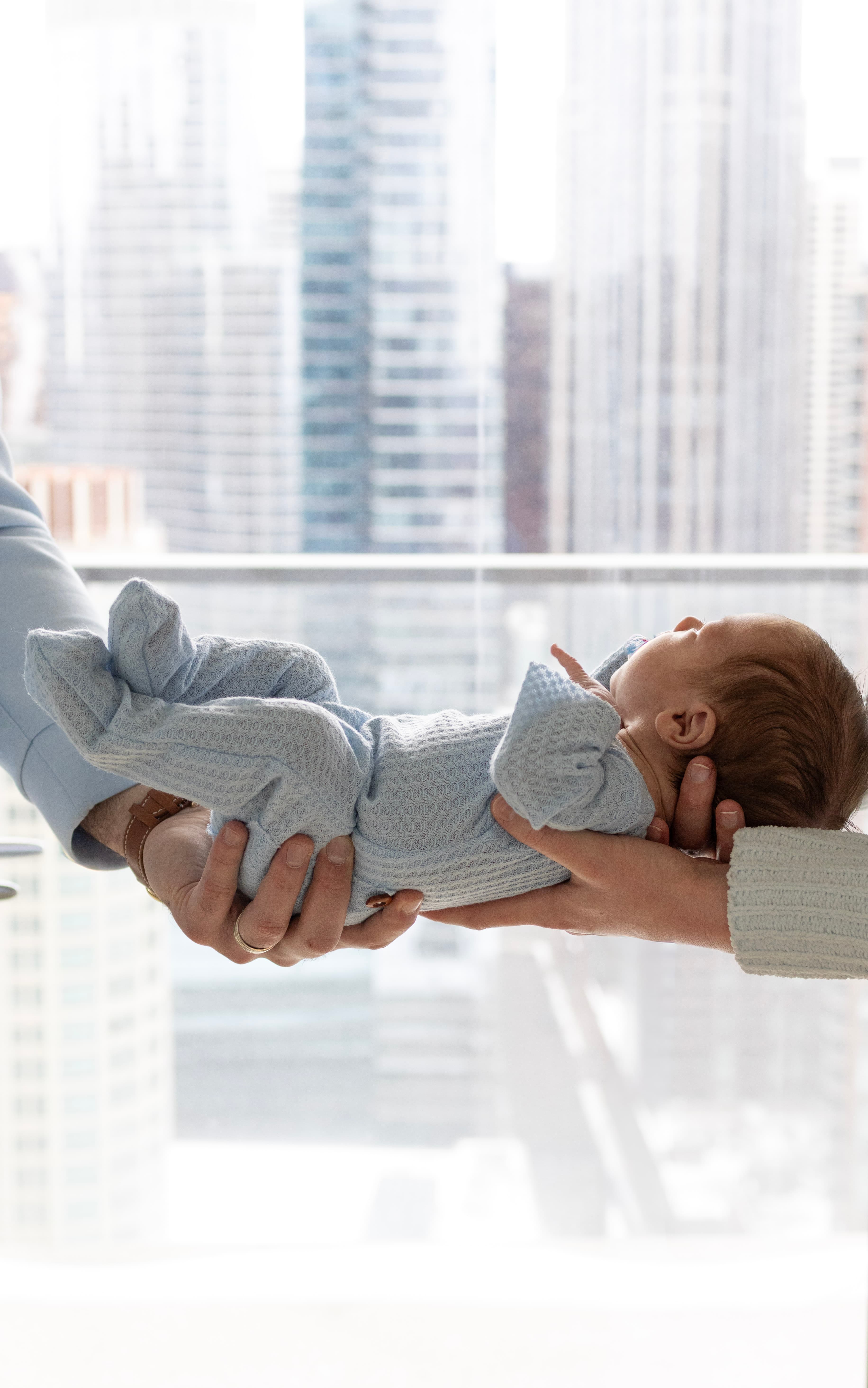 Newborn baby held by parents with city skyline — newborn photography session