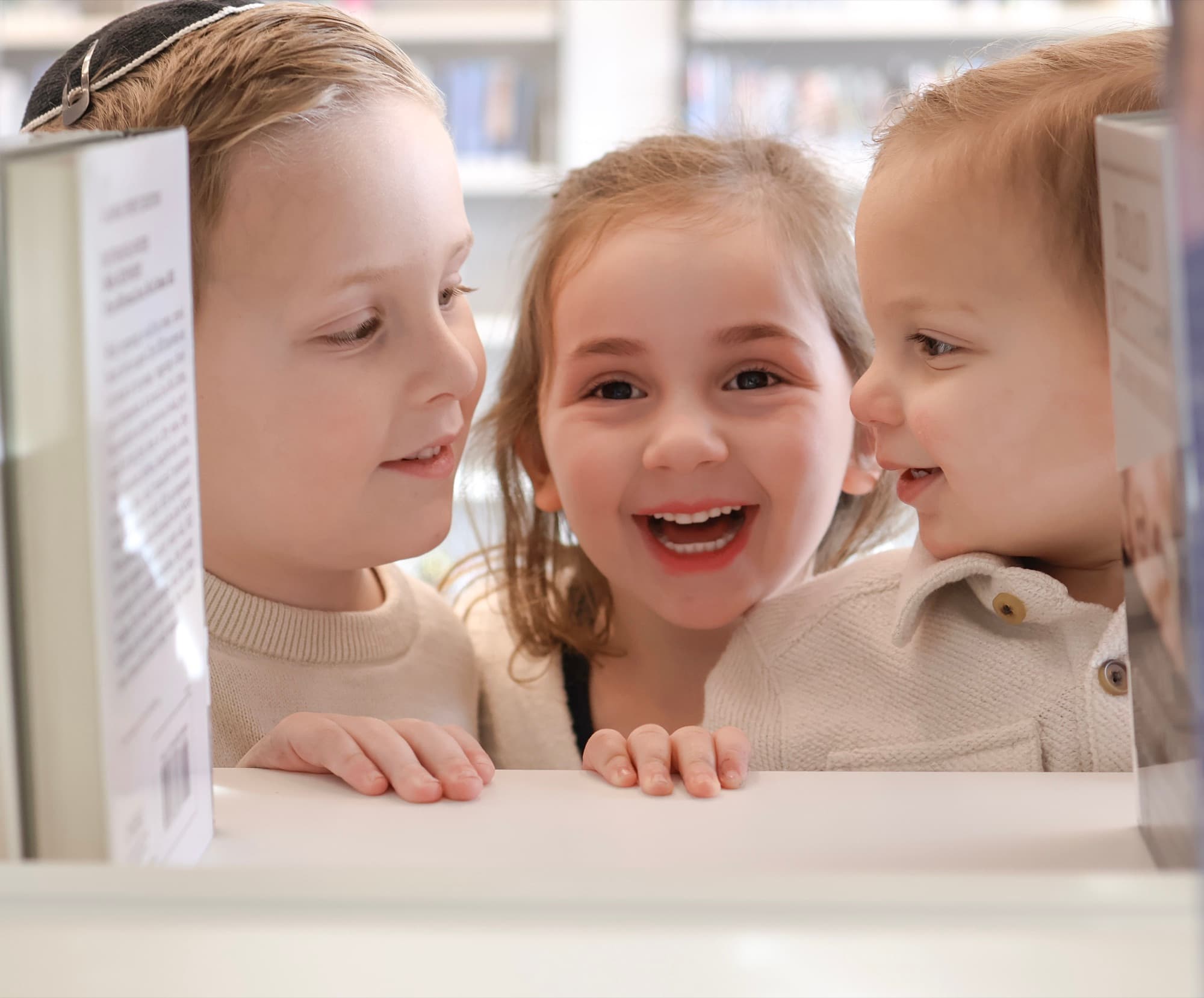 Three kids peeking between library books — playful family photography Skokie