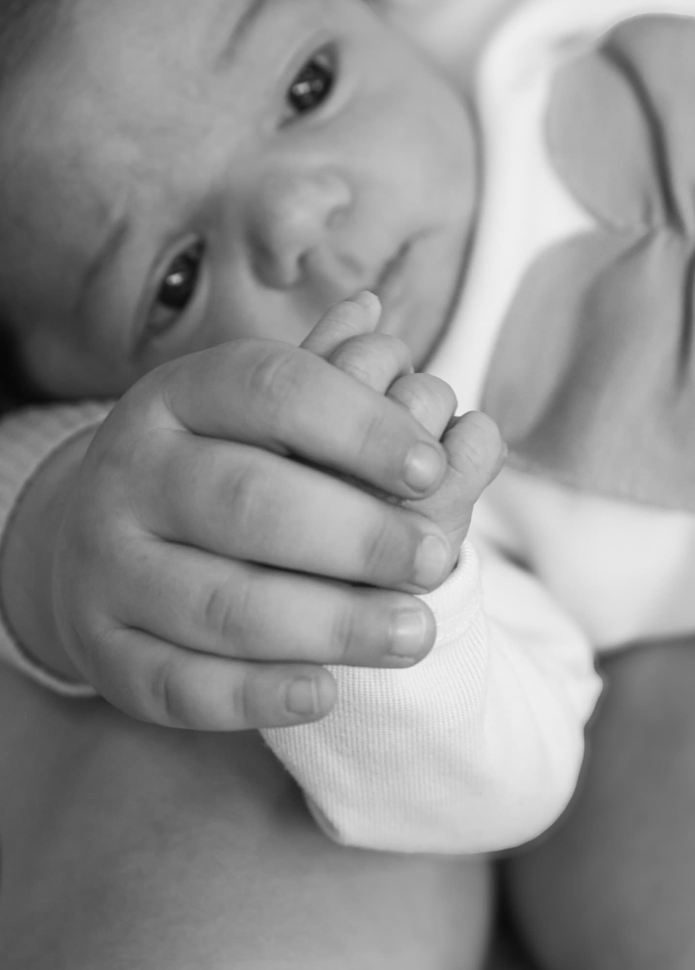 Newborn holding parent's finger — black and white detail