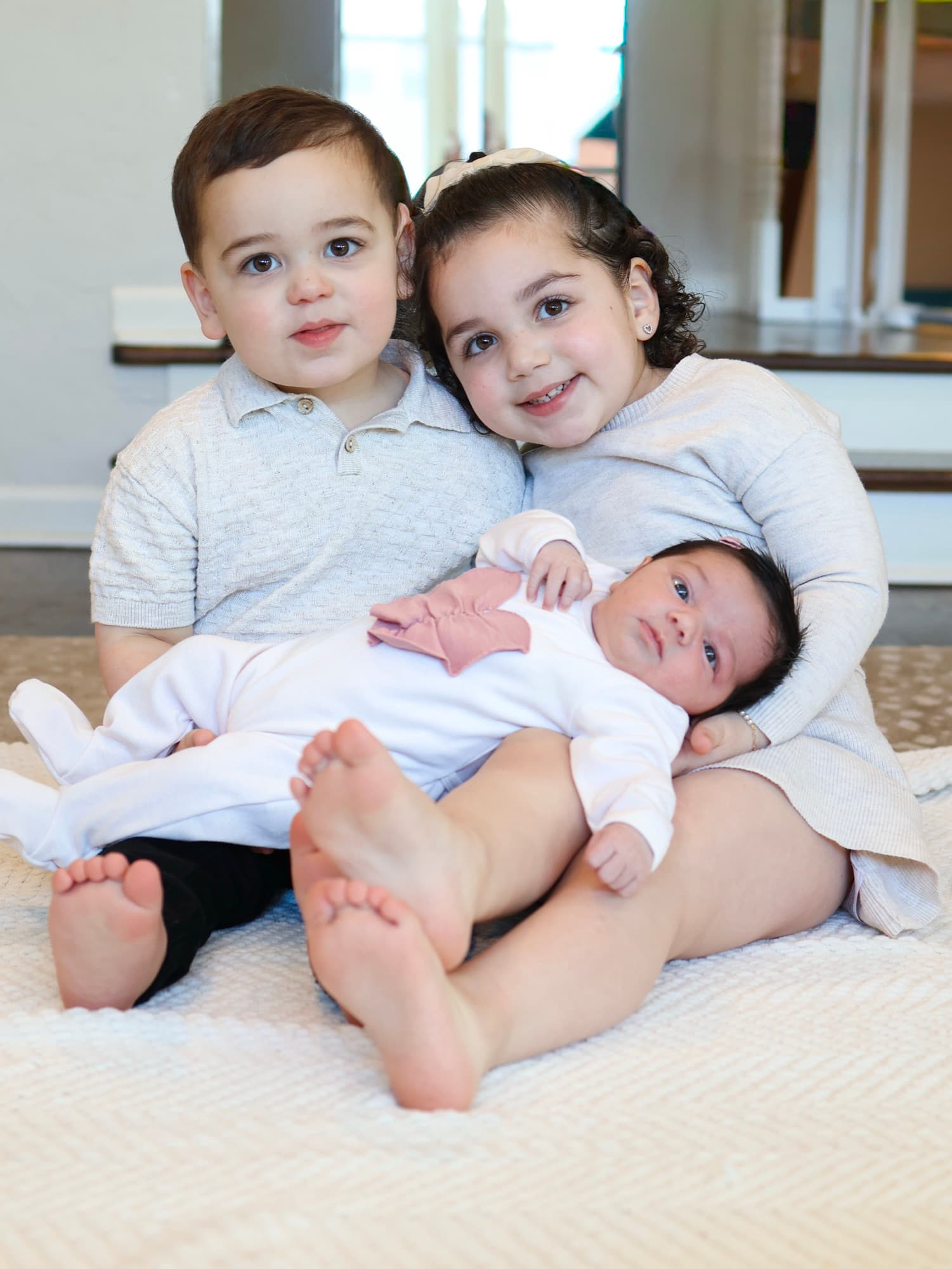 Siblings sitting with newborn baby on floor — lifestyle family