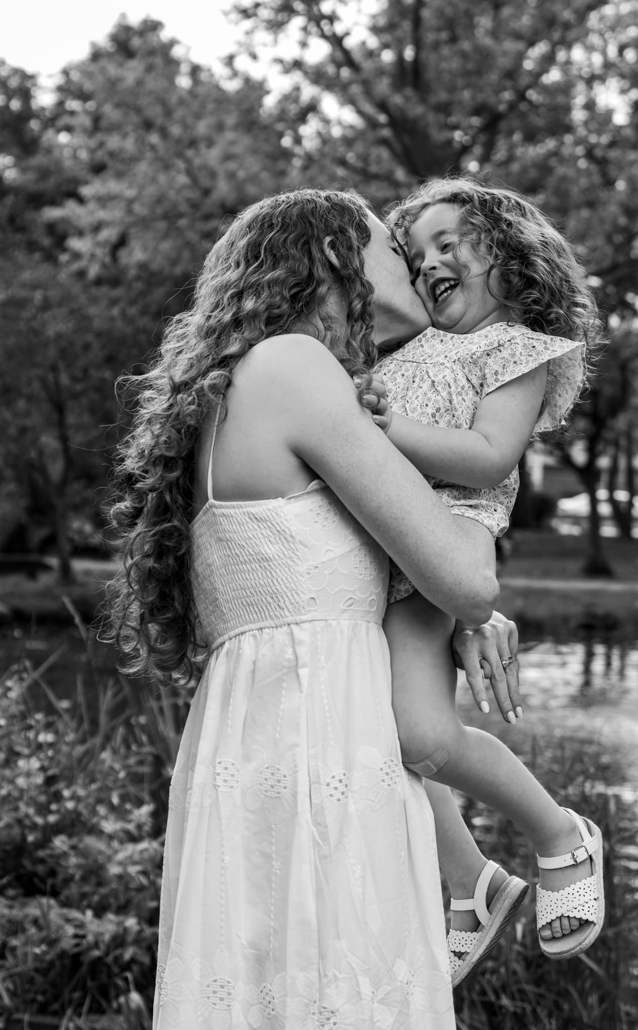 Joyful black and white moment of mom kissing laughing daughter at Keay Nature Center in Wilmette
