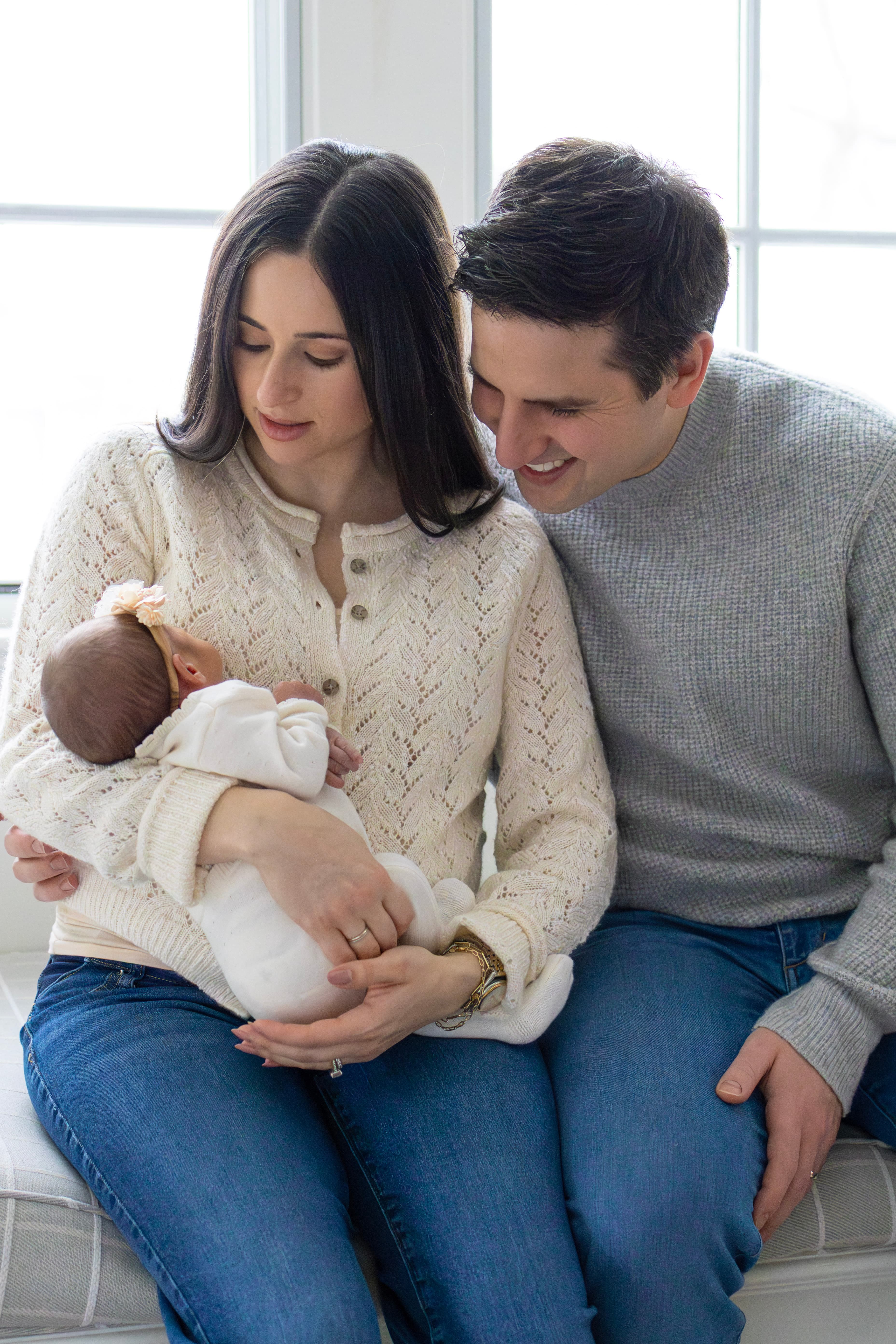 Parents holding newborn baby by window — natural light newborn photography