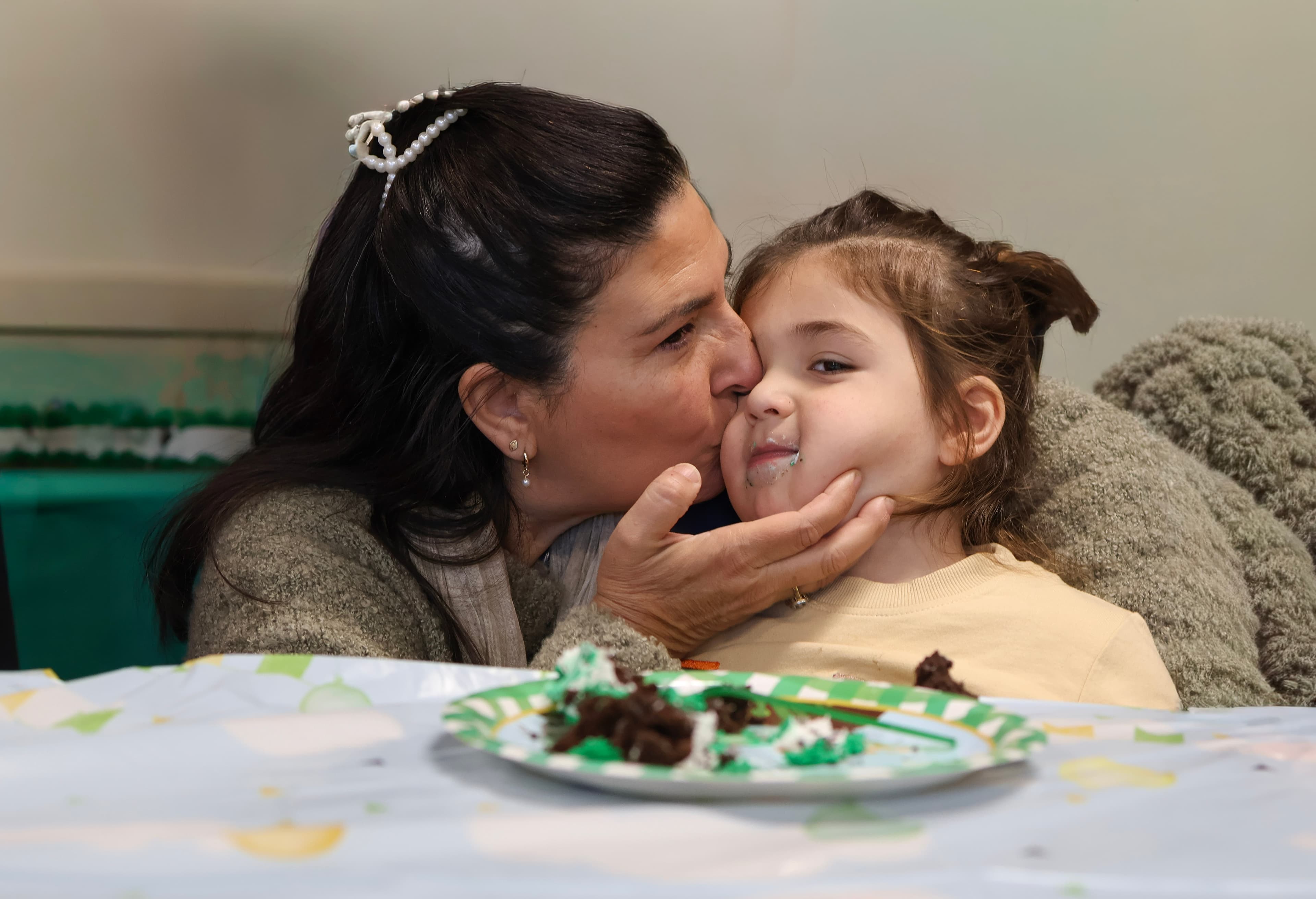 Grandmother kissing birthday girl with cake on her face — emotional milestone photography